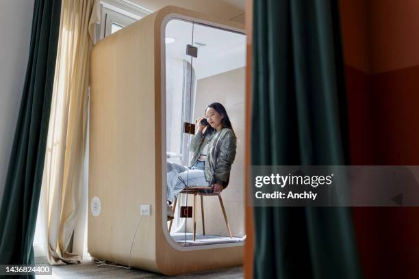 a young businesswoman is using a phone booth to talk on the phone in her office - booth stock pictures, royalty-free photos & images