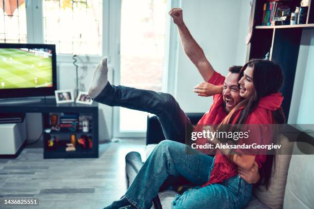 couple riant et acclamant pendant un match de sport à la télévision - watching soccer excited home photos et images de collection