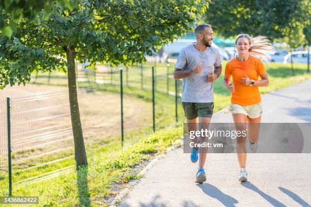 smiling sportive young couple jogging in urban park and talking - couple running stock pictures, royalty-free photos & images