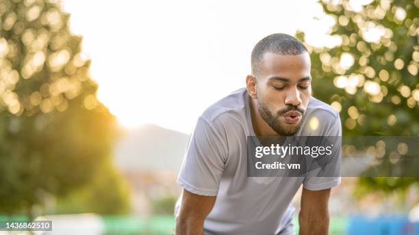 joven deportista afroamericano agachándose, respirando profundamente después de un entrenamiento fuera de curso - breathing exercise fotografías e imágenes de stock