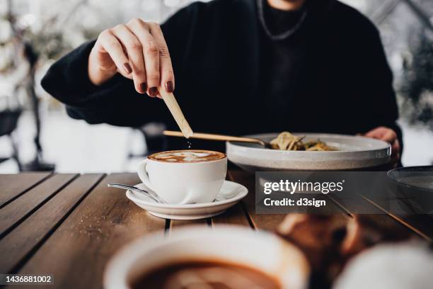cropped shot, mid-section of young woman having lunch in an outdoor restaurant, adding brown sugar to coffee on the dining table. eating out lifestyle - colocar imagens e fotografias de stock