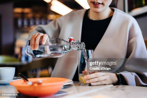 close up of young asian woman pouring water into glass at restaurant. healthy lifestyle and stay hydrated - 3 d glasses foto e immagini stock