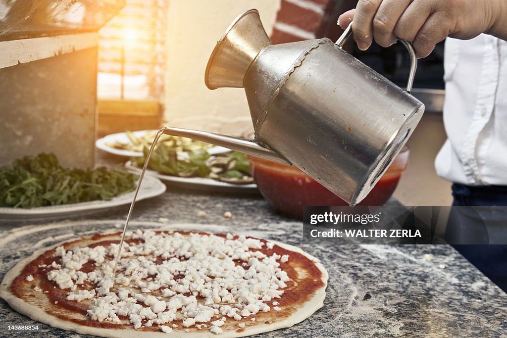 Chef pouring oil on uncooked pizza