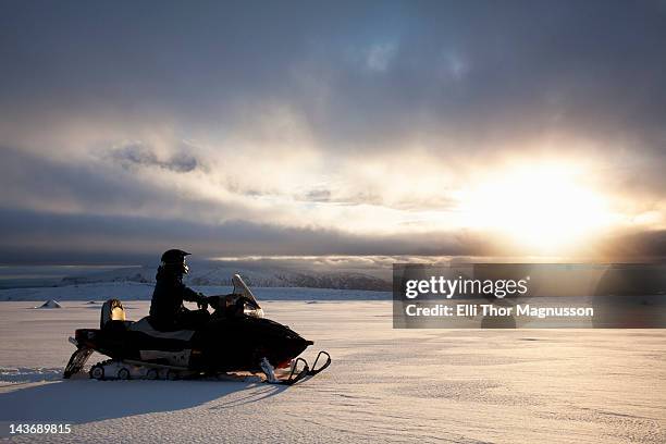 man driving snowmobile in snowy field - snowmobile stock pictures, royalty-free photos & images