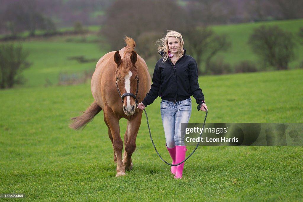 Teenage girl walking horse in field