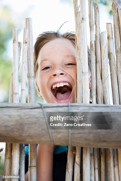 close up of boy smiling behind fence - boy freckle stock pictures, royalty-free photos & images
