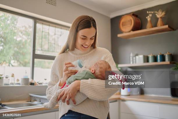 mother feeding her baby a bottle of milk with love, care and happiness while standing in the kitchen. happy, smile and newborn child drinking infant formula from his mom in their modern family home. - infant formula stock pictures, royalty-free photos & images