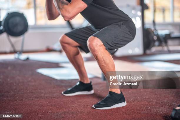 fokussierter kaukasischer männlicher athlet, der kniebeugen im fitnessstudio macht - hockend stock-fotos und bilder