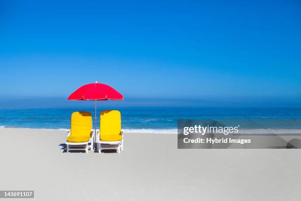 empty lawn chairs and umbrella on beach - strand liegestuhl stock-fotos und bilder