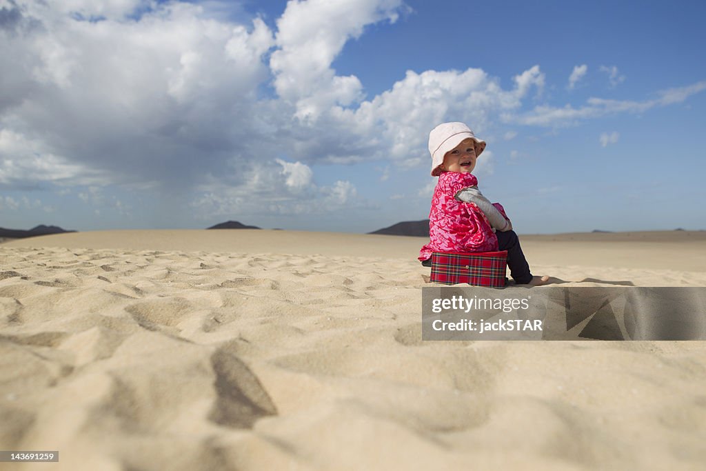 Toddler sitting on suitcase on beach