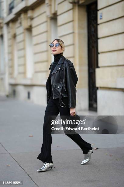 Emy Venturini wears black cat eyes sunglasses, gold earrings, a black ribbed wool turtleneck pullover from Intimissimi, a black shiny leather biker...