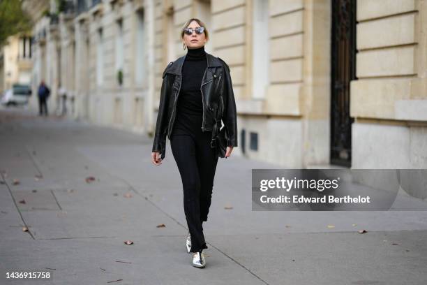 Emy Venturini wears black cat eyes sunglasses, gold earrings, a black ribbed wool turtleneck pullover from Intimissimi, a black shiny leather biker...