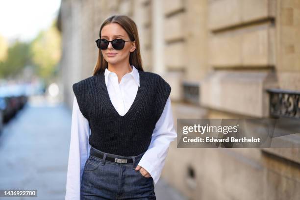 Diane Batoukina wears black sunglasses, a white shirt, a black V-neck / sleeveless wool pullover, a black shiny grained leather Kelly small belt from...