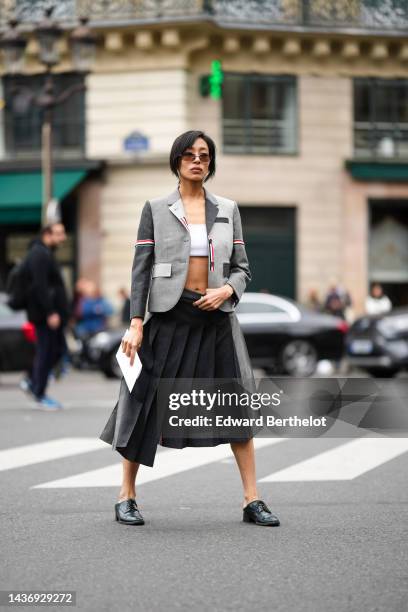 Guest wears brown sunglasses, a white shoulder-off / cropped top, a bicolored gray yoke with red striped print pattern blazer jacket from Thom...