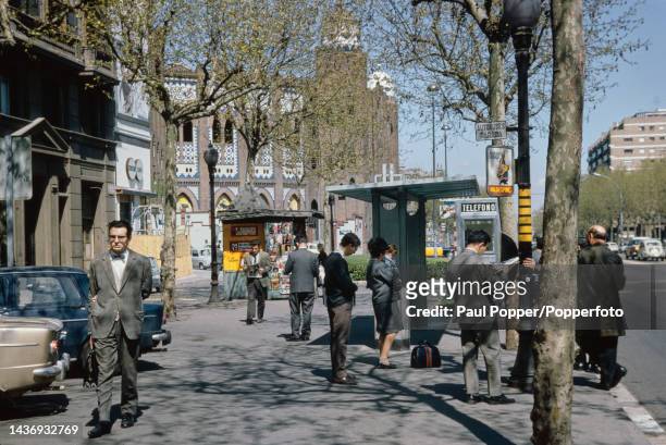 Pedestrians walk along Gran Via with, behind, La Monumental bullring in the centre of Barcelona, capital city of Catalonia in Spain in April 1968.
