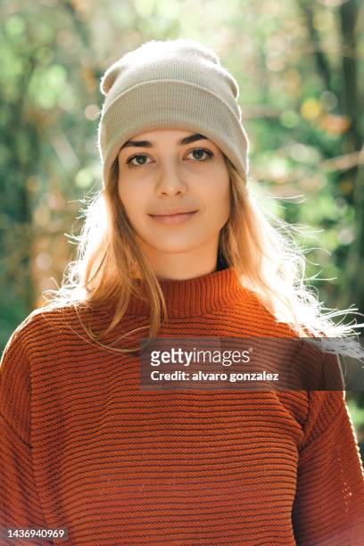 portrait of a woman in sweater and hat looking at camera while standing outdoors in nature. - november 22 stock pictures, royalty-free photos & images