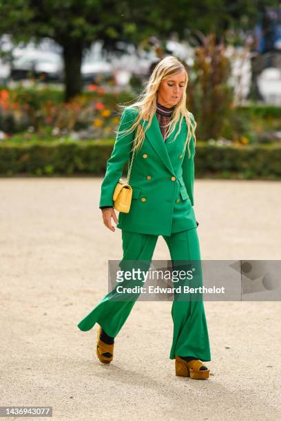 Guest wears gold earrings, a brown / black / pink glitter high neck pullover, a green with gold buttoned blazer jacket, green large suit pants, a...