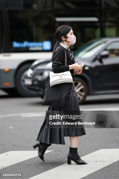 Guest wears a white and black print pattern silk scarf, a black cardigan, a white shiny leather Hourglass shoulder bag from Balenciaga, a black...