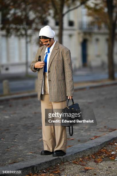 Guest wears a white scarf on the head, black sunglasses, a blue t-shirt, a white shirt, a brown and beige checkered print pattern blazer jacket,...