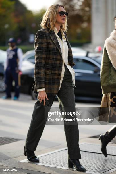 Guest wears black sunglasses, a black t-shirt, a white latte silk shirt, a brown and black checkered print pattern wool blazer jacket, black denim...