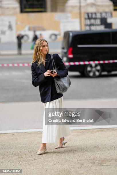 Guest wears a black blazer jacket, a white pleated / accordion long skirt, a black and gray print pattern in coated canvas shoulder bag from Goyard,...