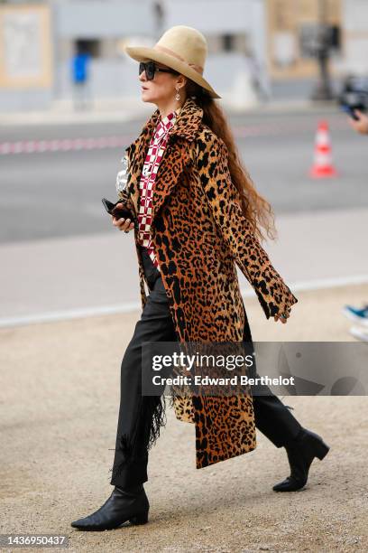 Guest wears a beige felt wool hat, black sunglasses, a white and red print pattern shirt, a brown with black leopard print pattern long fur coat,...