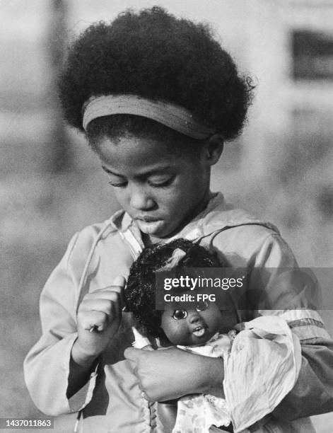 Girl combing the hair of 'Baby Nancy', the doll she is holding, in Los Angeles, California, circa 1970. 'Baby Nancy' was manufactured by Shindana...