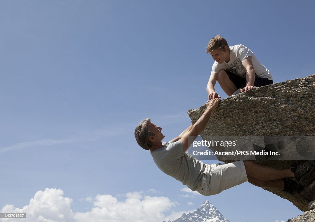 Man climbing a rock while his son tickles his hand