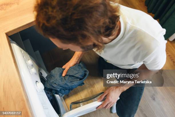 a young man is throwing things into the washing machine. domestic quarrel. problems of cleanliness in the house. cleaning company. vivid negative emotions of a man. - hair dryer stock photos et images de collection