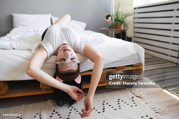 girl in pajamas on the bed in a cosmetic face mask with cucumbers on her eyes. care for yourself. natural cosmetics. morning care. fabric mask. facial skin care to preserve youth. - face mask beauty product - fotografias e filmes do acervo