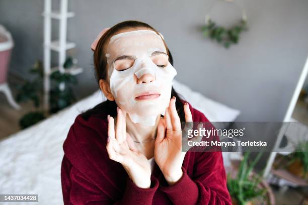 the girl put on a cosmetic cloth face mask. personal care. cosmetic face mask. fabric mask. facial skin care to preserve youth. - フェイスパック ストックフォトと画像