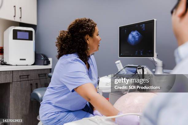 vista sobre o ombro da técnica de ultrassom feminino assistindo bebê na tela - ultrasound scan - fotografias e filmes do acervo