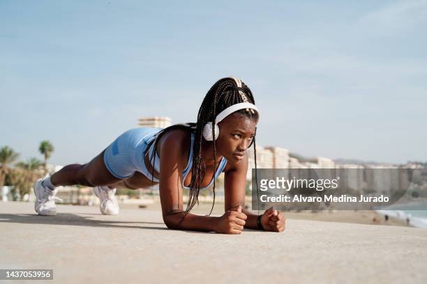 young black female athlete focused on doing plank on her arms on a stone wall. - body building exercises stock pictures, royalty-free photos & images