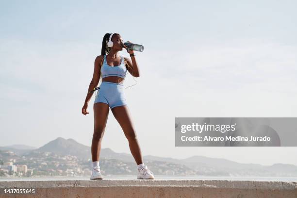 young black female athlete drinking water after jumping rope with sky and mountains in background. - sport drink stock pictures, royalty-free photos & images