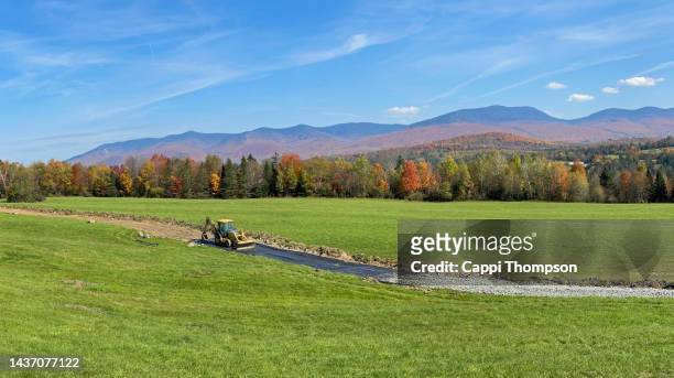 tractor with back hoe and front end loader installing new driveway or road across field in lancaster, new hampshire usa - new zealand and farm or rural stock-fotos und bilder