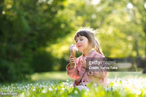 glückliches kind, das eis isst, sitzt auf dem gras in einem parkporträt. glückliche kindheit. - baby spielt mit essen stock-fotos und bilder