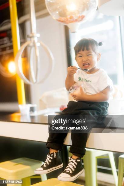 positive emotion asian baby girl enjoy eating frozen yogurt - joghurtbecher stock-fotos und bilder