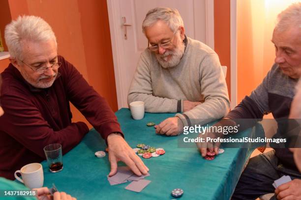eine kleine gruppe von senioren nimmt an einer gesellschaftlichen veranstaltung teil, indem sie karten spielt. - card game mature people stock-fotos und bilder