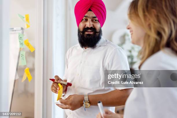 startup professionals brainstorming with notes on a glass wall in office - sikhism stock-fotos und bilder