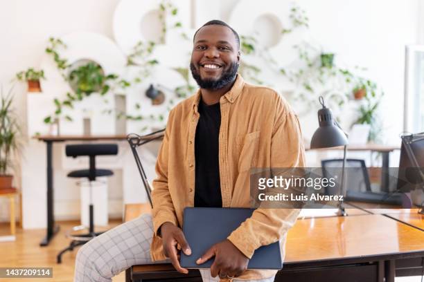 portrait of a smiling african businessman holding laptop at coworking office - portrait man business stockfoto's en -beelden