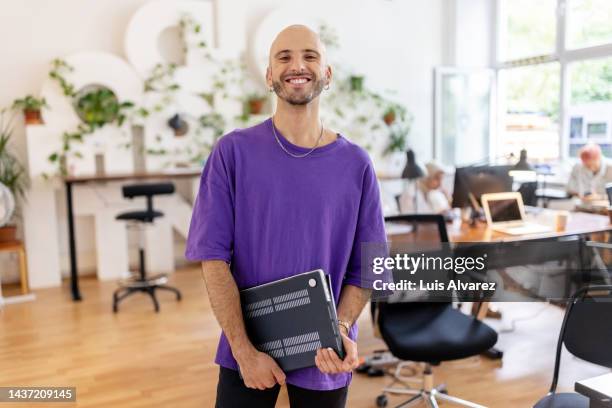 portrait of a happy bald businessman standing in office holding laptop - bald man foto e immagini stock