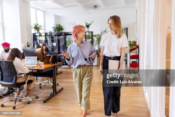 two woman business professionals walking through the office and discussing work - businesswear stock pictures, royalty-free photos & images