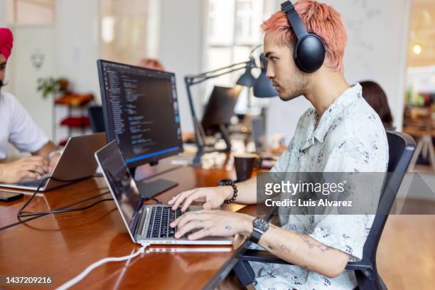 young man wearing headphones working on computer at startup office - wissenschaft und technik stock-fotos und bilder