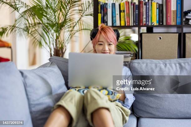 asian with headphones sitting on sofa working on laptop at office - schriftsymbol stock-fotos und bilder