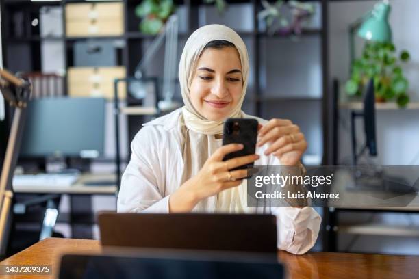 happy young muslim woman using mobile phone in office - arab and mobile stock pictures, royalty-free photos & images