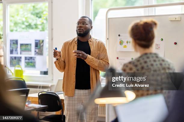 young man explaining the project to team at coworking office - unternehmer stock-fotos und bilder