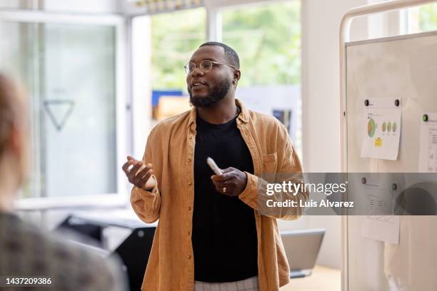 african man giving a presentation to the team at coworking office - analysieren zusammenarbeit stock-fotos und bilder