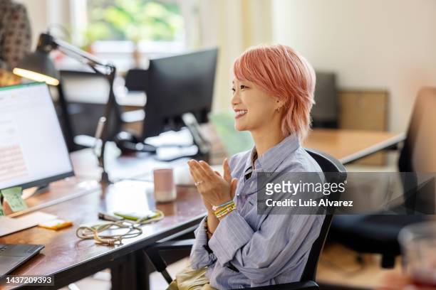 happy asian businesswoman sitting at her desk and clapping hands during meeting - pink hair stock pictures, royalty-free photos & images