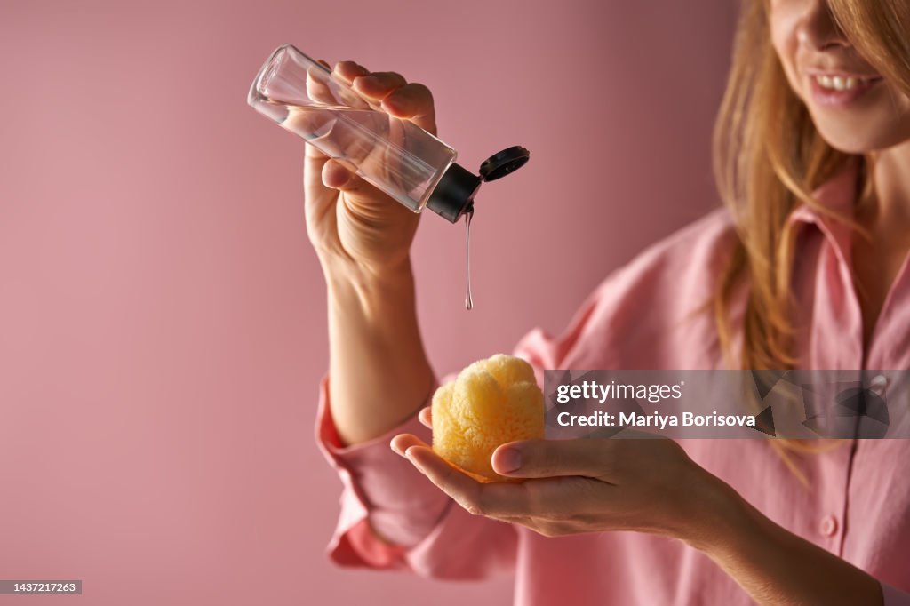 A girl in pink pours a wash gel on a natural sea sponge.