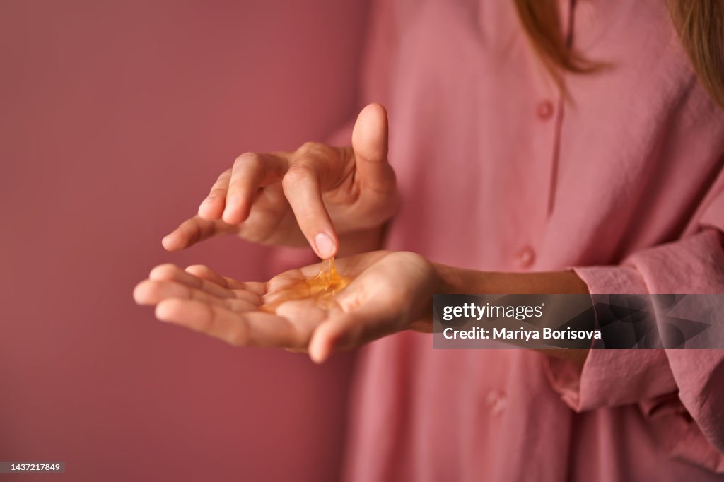 A girl in pink touches a gel cosmetic in her palm with her finger.